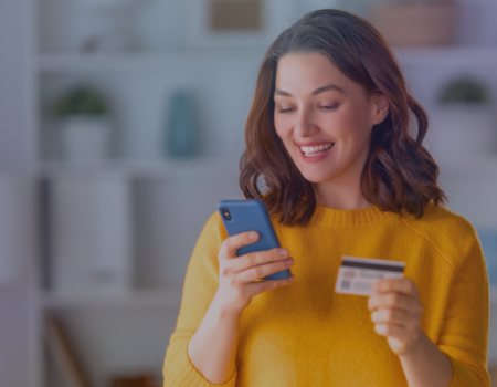 woman on a yellow jumper holding her phone and her credit card and smiling