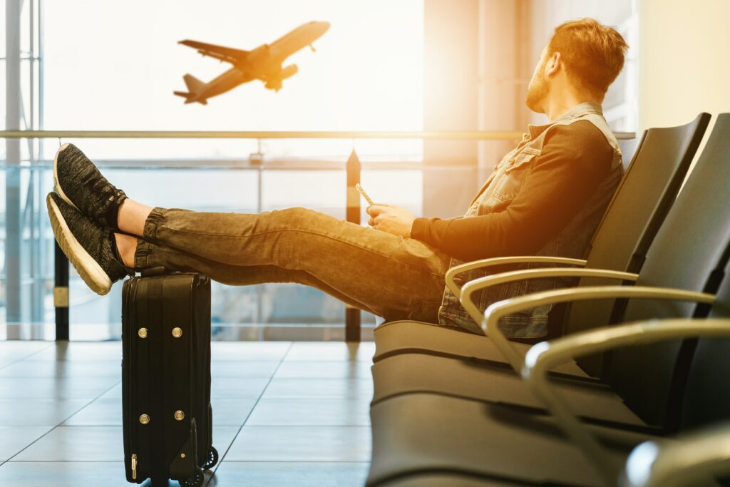 Man sitting in an airport with his feet on hiss luggage bag. An airplane passes in the back