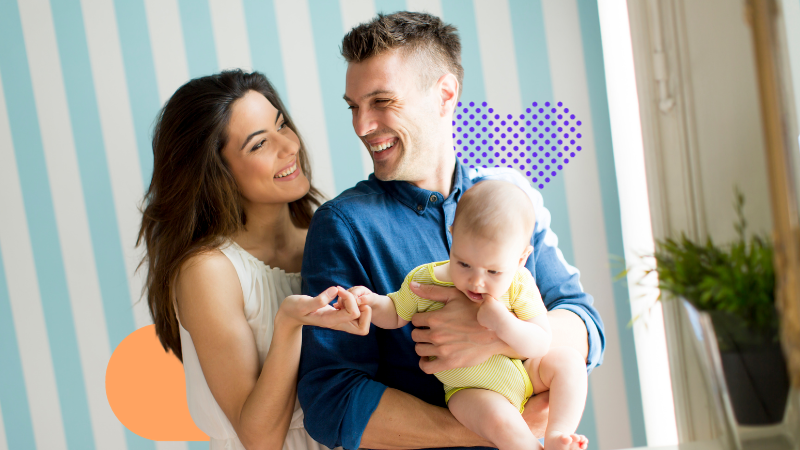 A woman smiling to a man who is holding a baby while smiling back at her. Family