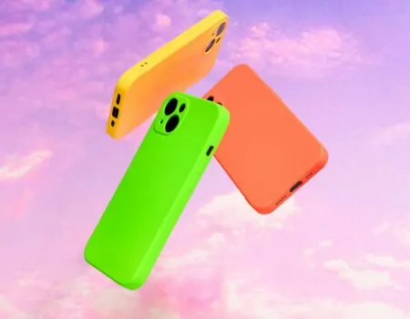 Three bright-coloured phones in yellow, orange and neon green floating in a circle against an abstract purple, cloudy sky.