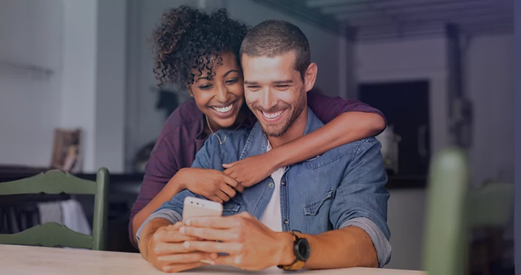 a couple of a man and a woman looking at a phone that the man is holding and smiling